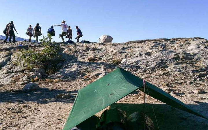 A group of outward bound students stand in a circle and stretch. There is a tarp shelter in the foreground.